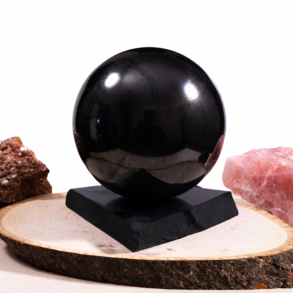 Black polished shungite sphere on square base, displayed on a natural wood slab