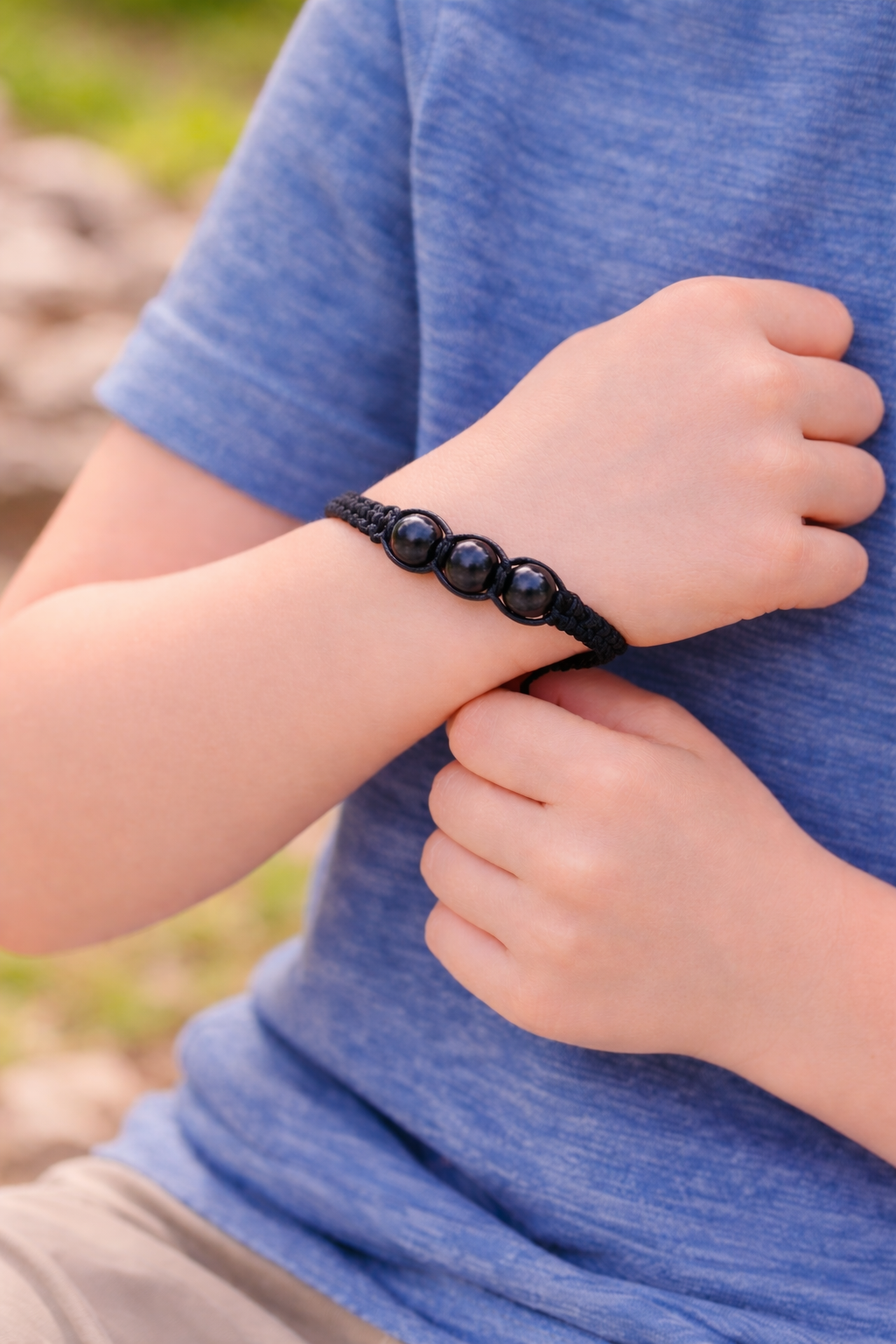 A child wearing an adjustable black woven cord bracelet featuring three polished round shungite  beads.