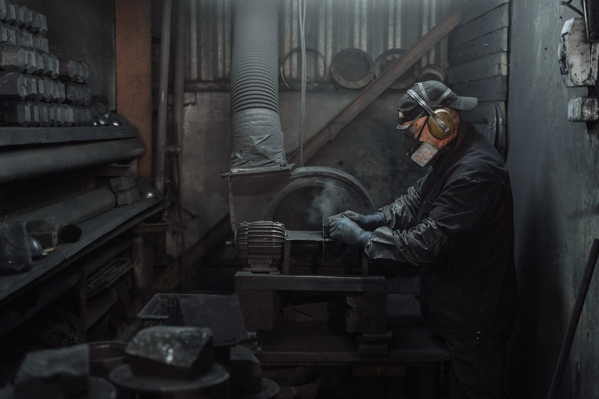 Artisan wearing protective gear while precision crafting a black Shungite sphere harmonizer in a dark industrial workshop