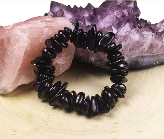 An alternate close-up view of a black shungite beaded chip boho bracelet resting on a wooden slice.
