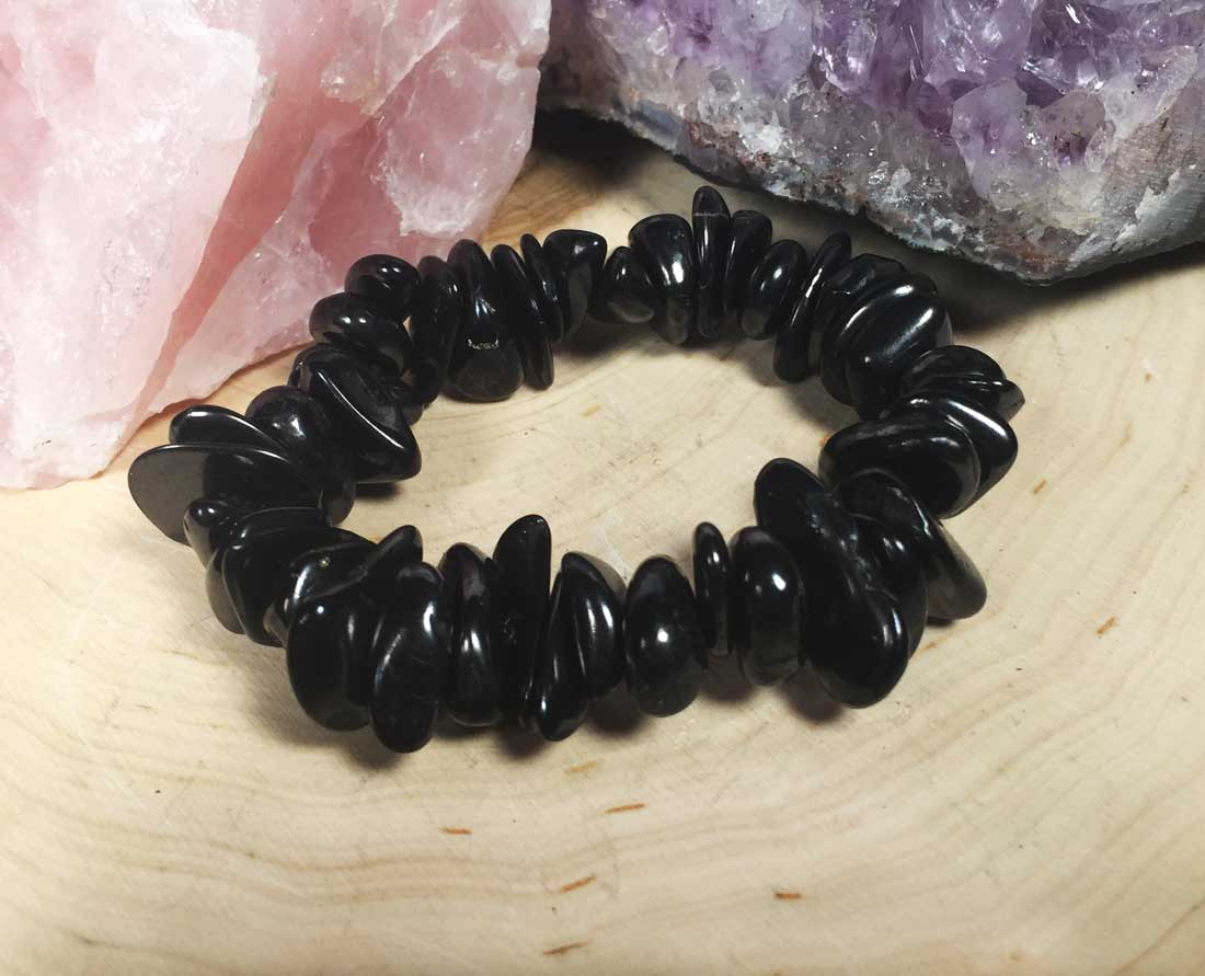 A black shungite beaded chip boho bracelet displayed on a wood slice.