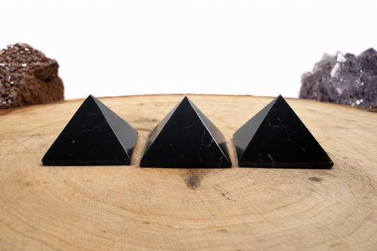 A 3-pack set of mini polished black Shungite pyramids arranged in a row on a round natural wood slice.