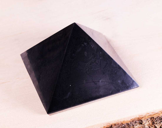 Polished authentic Karelian shungite pyramid showcasing natural stone texture on a live edge wood surface.