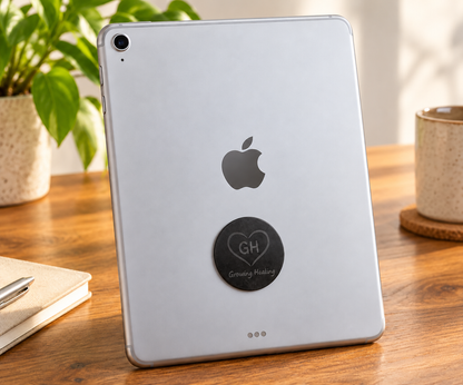 Premium black Shungite circular plate attached to the back of a silver tablet below the Apple logo on a wooden desk.