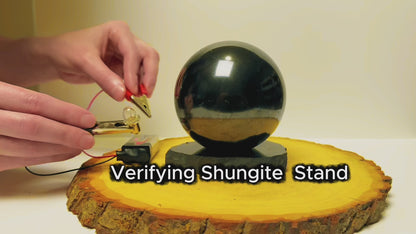 Testing the electrical conductivity of a black shungite sphere and display stand.