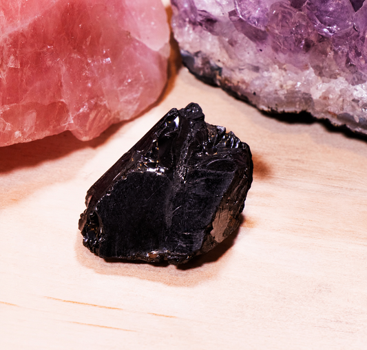 Close-up view of a single raw Elite Noble Shungite medium-sized stone highlighting its unique carbon-rich reflective surface and natural glassy texture.
