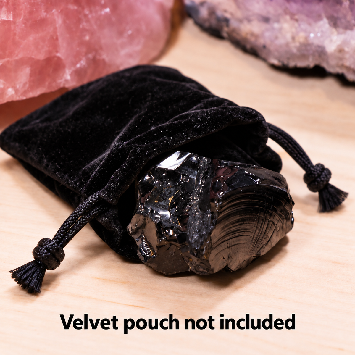 A large, raw elite noble shungite crystal with a metallic silver sheen resting in a black velvet drawstring bag on a wooden base with overlay text reading 'Velvet pouch not included'