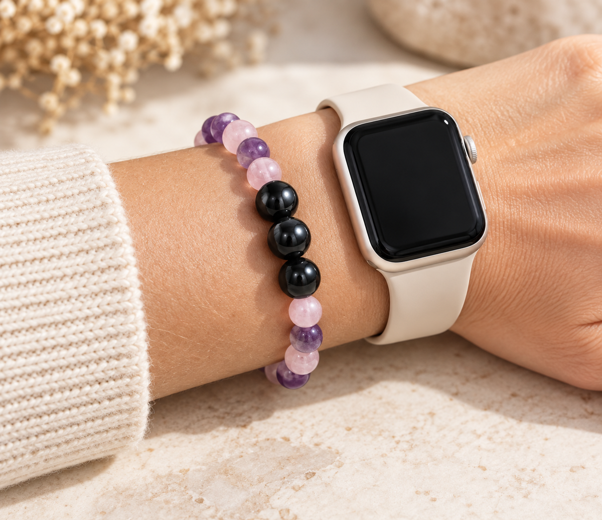 A beaded crystal bracelet featuring three polished black Shungite beads, light pink rose quartz, and purple amethyst spheres worn next to a smart watch on a wrist.