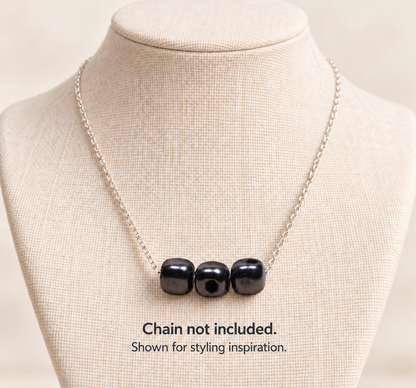 Three black Shungite cube beads styled horizontally as a pendant on a silver chain displayed on a jewelry bust. Text reads: Chain not included. Shown for styling inspiration.