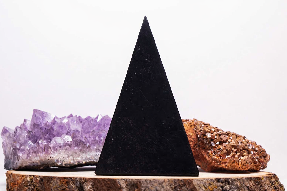Front view of a tall Golod Shungite pyramid on a piece of wood with crystal display.