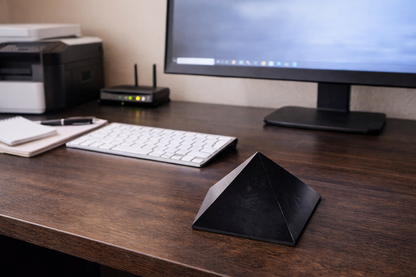 Large authentic Karelian shungite pyramid positioned as a digital grounding anchor on a wooden desk with a computer keyboard and monitor backdrop.