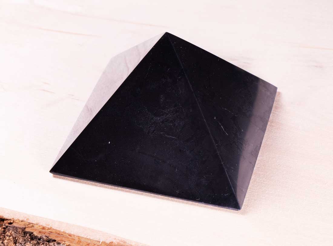 Polished authentic Karelian shungite pyramid viewed from an angle showcasing its natural matte black texture.
