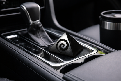 A polished black shungite pyramid with an engraved spiral swirl design placed in a car center console next to the gear shift.