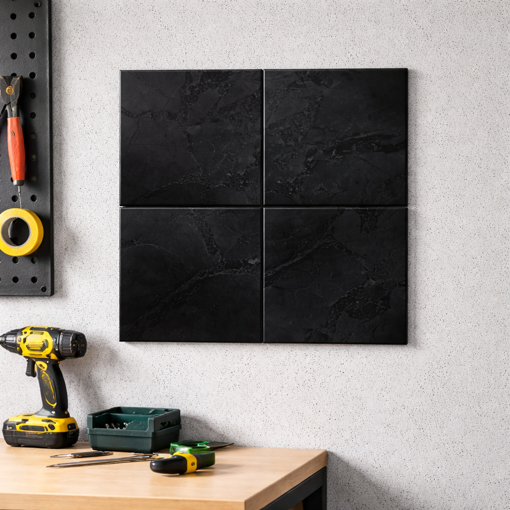 Four square black shungite tiles arranged in a larger square grid pattern on a light textured wall in a garage workspace setup above a wooden workbench with tools.